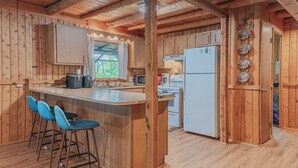 A wooden cabin interior with a kitchen area, bar stools, and a refrigerator.