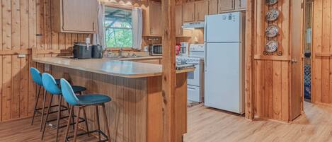 A wooden cabin interior with a kitchen area, bar stools, and a refrigerator.