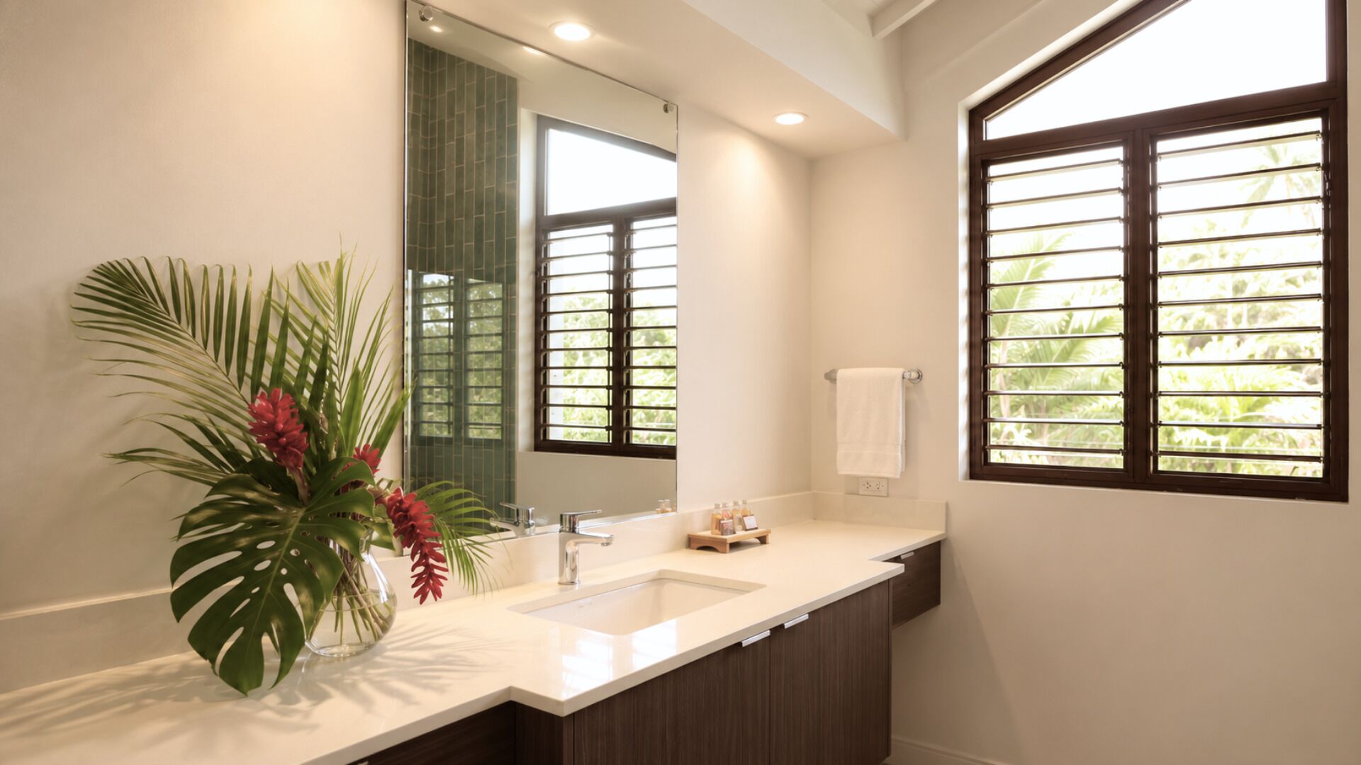 A bathroom with a white sink, a mirror, a potted plant, and a window with blinds.