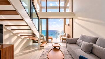 Un intérieur moderne avec un escalier menant à un balcon donnant sur la mer, un canapé et une table basse.