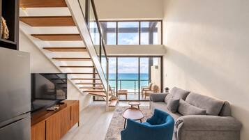 Un salon moderne avec un escalier menant à un balcon d’où l’on a vue sur la mer.