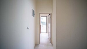 Um corredor estreito com uma porta no final, dando acesso a um quarto claro.