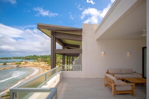 Ein moderner Balkon mit Meerblick, Holzmöbel und Glasgeländer.