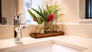Ein Waschtisch mit einem modernen Wasserhahn, eine Glasvase mit roten Blumen und drei Toilettenartikel auf einer Holzschale.