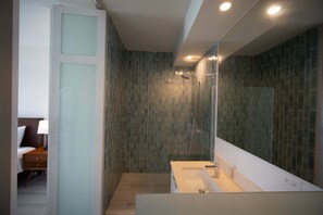 Uma casa de banho moderna com cabine de duche em vidro, lavatório branco e um espelho grande.