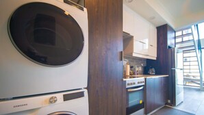 Een kleine keuken met een wasmachine, oven en uitzicht op buiten.