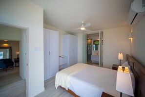 Ein Hotelzimmer mit Bett, Nachttisch, Lampe, Deckenventilator und einem durchgegangene Tür sichtbaren Badezimmer.