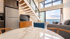 A modern interior with a kitchen, dining area, and a staircase leading to a balcony with a view of the sea. - Bessa | Beachfront 2BR Loft, Private Roof Terrace ➠ U80 (Oracabessa)