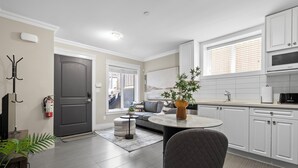 A modern kitchen with white cabinets, a dining area with a round table and chairs, and a living room with a sofa and a plant. - Beautiful 2 bedroom 1 bathrom (Burnaby)