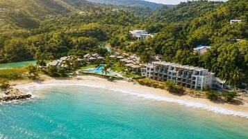 Un complexe hôtelier situé en bord de mer, doté d’une piscine et entouré d’une végétation luxuriante.