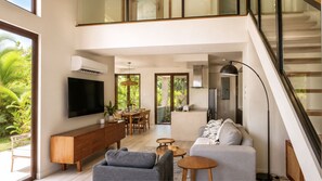A modern living room with a flat-screen TV, a sofa, a coffee table, and a dining area with chairs. - Bessa | Ocean View Villa | 2BR, Seaside Pool ➠ U52 (Oracabessa)