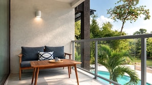 Ein Balkon mit Holztisch und einer Sitzecke, mit Blick auf einen Swimmingpool und viel Grün.