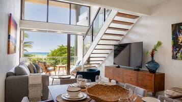 Un salon moderne doté d’un grand téléviseur, d’un coin repas et d’un escalier menant à un niveau supérieur.