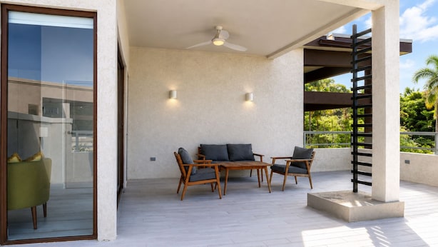 A covered outdoor seating area with a table and chairs, a ceiling fan, and a view of greenery. - Bessa | Riverfront 2BR Loft, Private Roof Terrace ➠ U11 (Oracabessa)