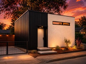 Un bâtiment moderne à deux étages, doté d’une façade sombre et d’une partie supérieure blanche, avec une petite fenêtre et une porte.