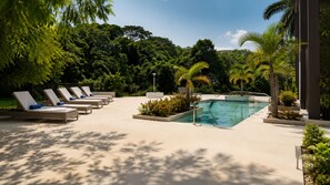 A poolside area with sun loungers and a swimming pool surrounded by lush greenery.