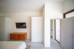 A bedroom with a bed, a wooden side table, a TV mounted on the wall, and a wardrobe.