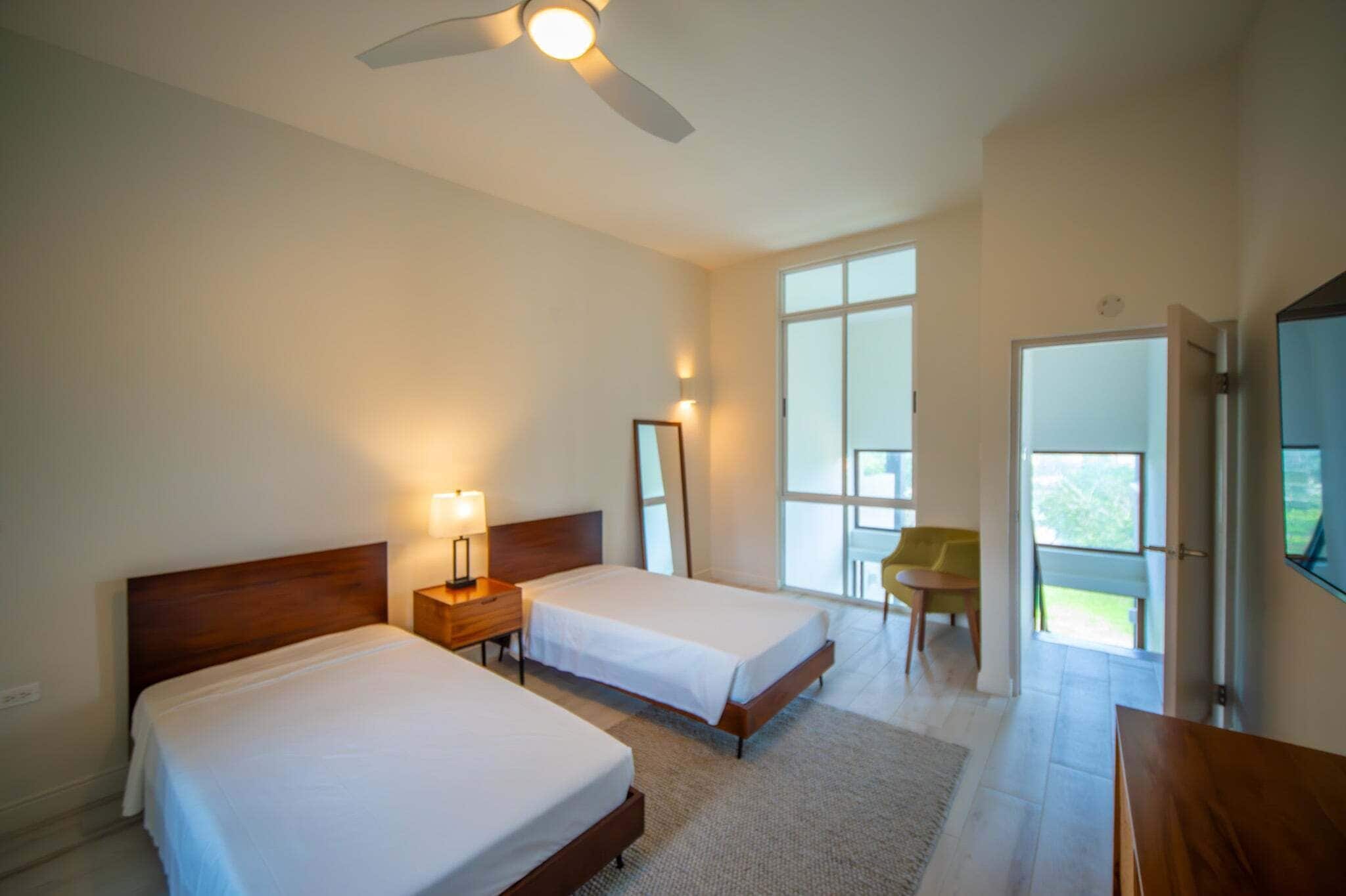 Ein Hotelzimmer mit zwei Betten, einem Deckenventilator, einem großen Fenster und einem Stuhl.