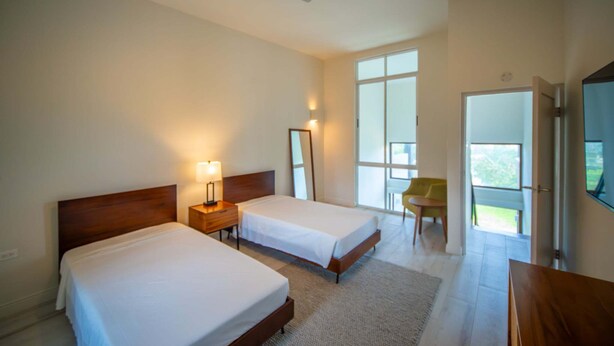A hotel room with two beds, a ceiling fan, a large window, and a chair. - Bessa | Riverfront 2BR | River, Sea & Pool ➠ U4 (Oracabessa)