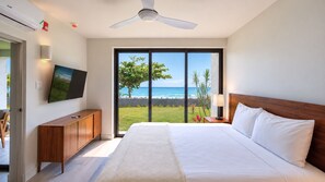A hotel room with a bed, a television, a ceiling fan, and a view of the ocean. - Bessa Riverside 2BR | River, Sea & Pool ➠ U4 (Oracabessa)