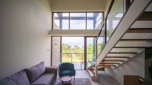 A modern interior with a sofa, armchair, and a staircase leading to an outdoor area. - Bessa | Riverfront 2BR | River, Sea & Pool ➠ U4 (Oracabessa)