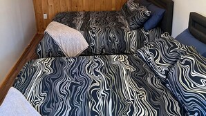 Une chambre avec des murs lambrés, un lit recouvert d’une literie à motifs et un ventilateur de plafond.