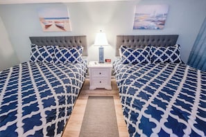 Una habitació d'hotel amb dos llits, una tauleta de nit amb una làmpada i obra d'art a les parets.