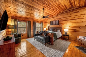 Ein Schlafzimmer in einer Blockhütte mit einem Bett, einem Schreibtisch, einem Stuhl, einem Fernseher und einem Fenster mit Vorhängen.