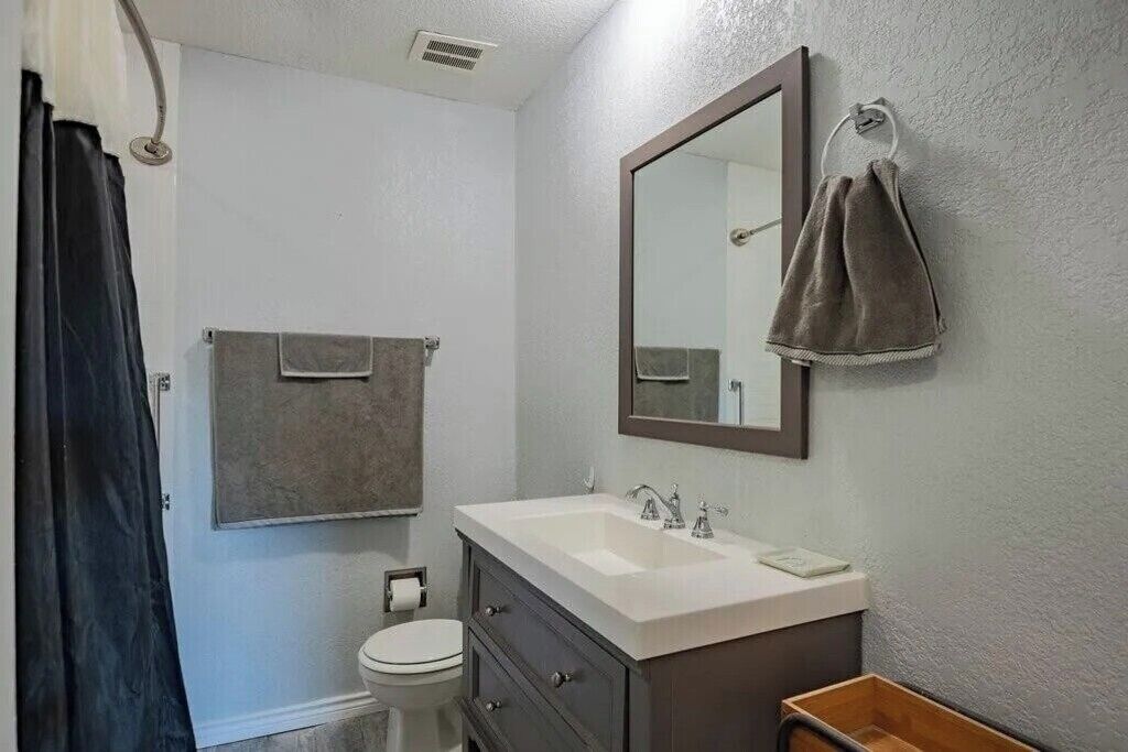 A bathroom with a white sink, dark cabinet, towel rack, and a mirror.