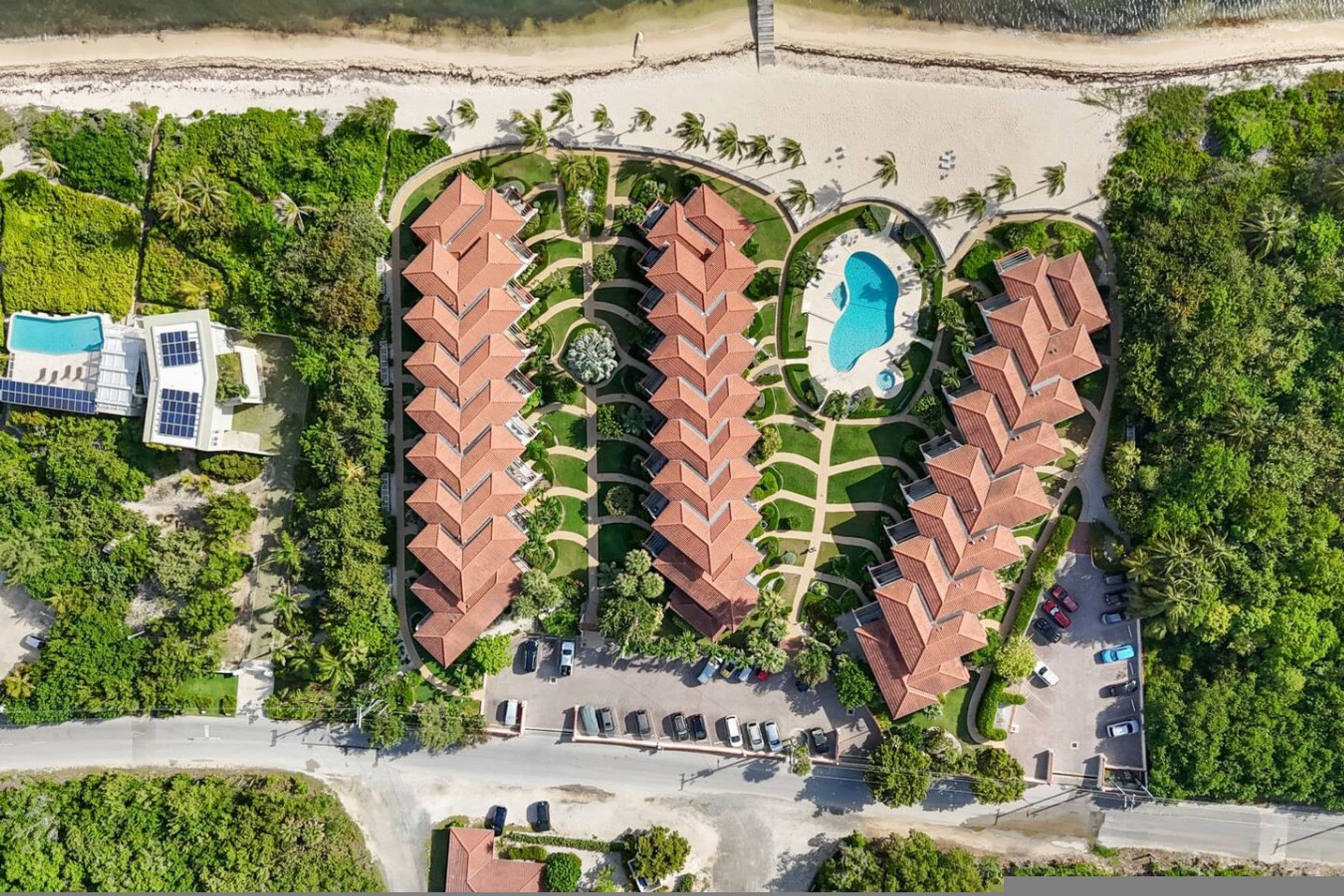An aerial view of a resort with multiple red-roofed buildings, a swimming pool, and a parking area.