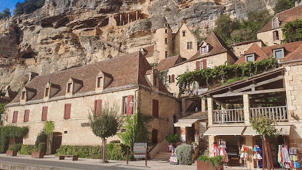 Un bâtiment en pierre doté d’un balcon, une enseigne indiquant « Le Petit Terrassé », et une vue sur une falaise rocheuse.
