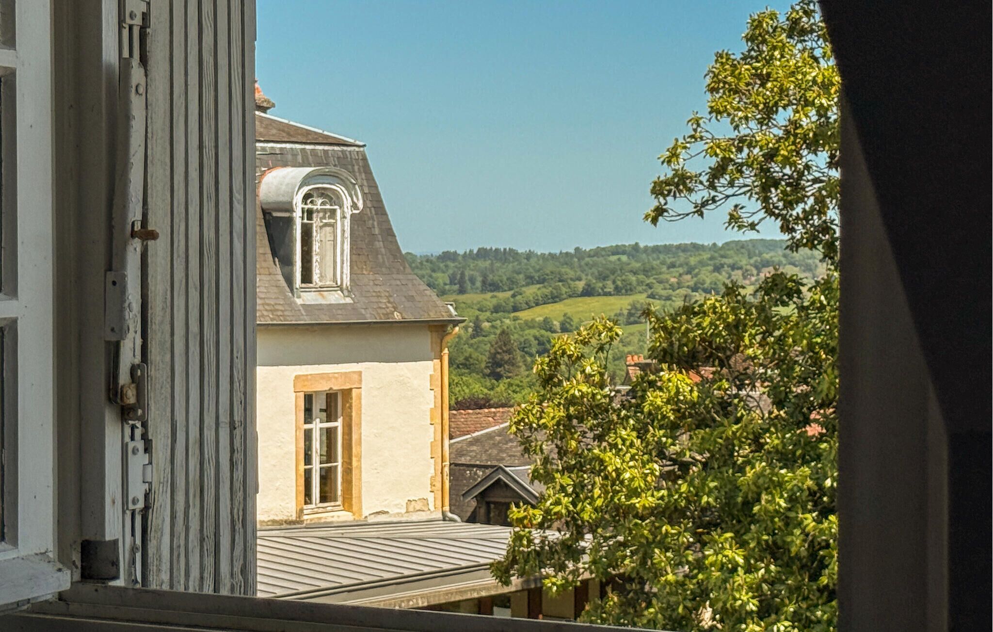 Une maison avec un toit en pente, une fenêtre et une vue sur un paysage verdoyant.