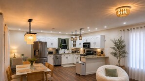 Una cocina moderna con armarios blancos, electrodomésticos de acero inoxidable y una zona de comedor con mesa y sillas.