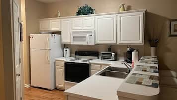 Una cocina compacta con muebles blancos, un microondas integrado, estufa y una pequeña zona de encimera.
