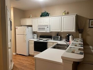 Una cocina compacta con muebles blancos, un microondas integrado, estufa y una pequeña zona de encimera.