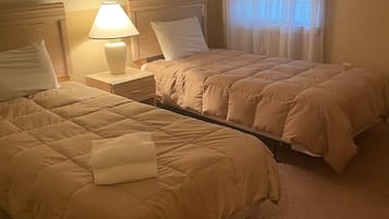 Habitación de hotel con dos camas, una mesita de noche con lámpara y una ventana con cortinas.