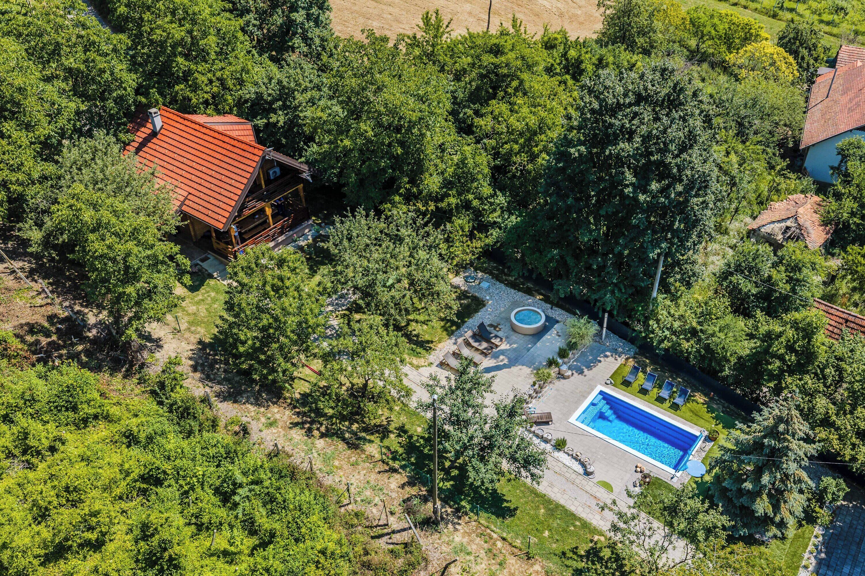 An aerial view of a property with a swimming pool, a red-roofed cabin, and surrounding greenery.