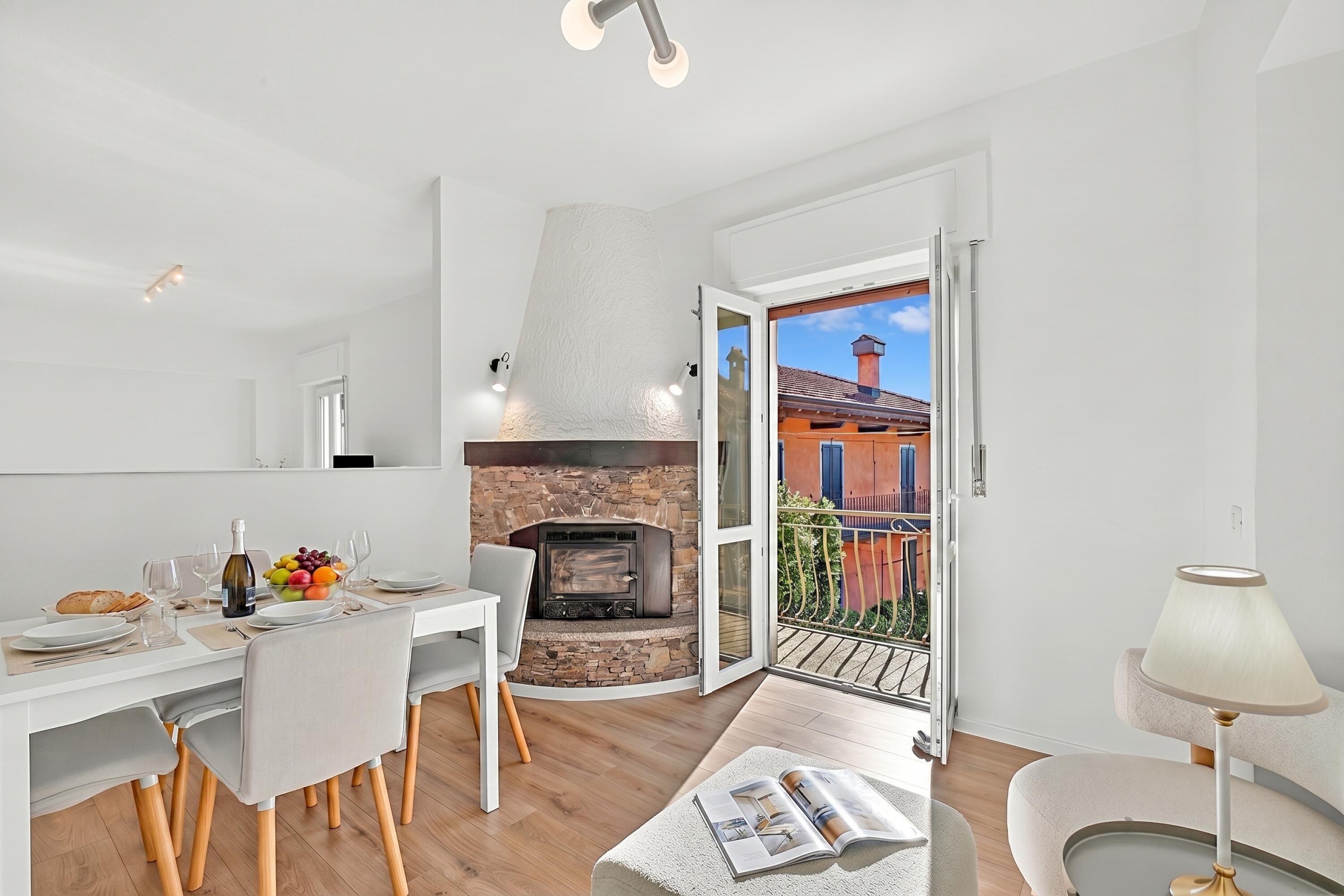 A modern kitchen with a stone fireplace, dining area with chairs, and a balcony with a view.