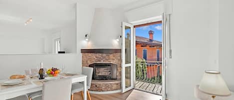A modern kitchen with a stone fireplace, dining area with chairs, and a balcony with a view.