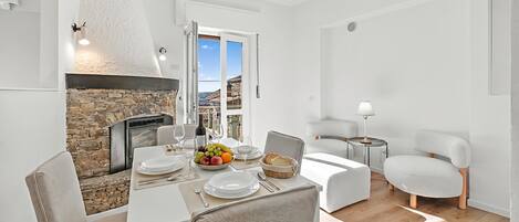A dining area with a stone fireplace, white furniture, and a view through an open door.