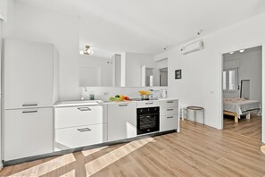 A modern kitchen with white cabinetry, a built-in oven, and a dining area with a small round table. - Quadrifoglio Stresa Hill with A/C and Sunny Balcony, Stresa, Italy (Stresa)