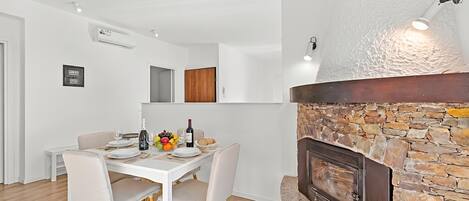 A modern dining area with a stone fireplace, white walls, and a wooden floor.