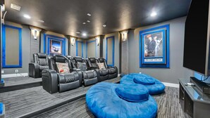 A home theater room with a large screen, multiple reclining chairs, and a carpeted floor. - Wilmington Grand Escape (Kissimmee)