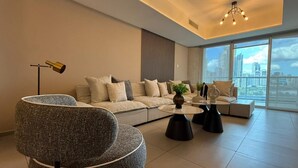 Un salon moderne avec un canapé, des fauteuils, une table basse et une vue sur la ville grâce à de grandes fenêtres.