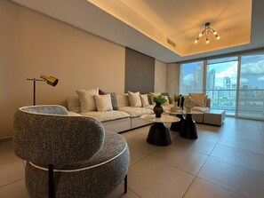 Ein modernes Wohnzimmer mit einer Couch, Sesseln, einem Couchtisch und Blick auf die Stadt durch große Fenster.