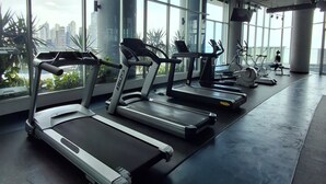 Une salle de sport équipée de tapis de course, de vélos d’exercice et dotée d’une grande fenêtre offrant une vue sur la ville.