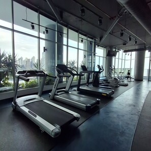 Ein Fitnessstudio mit Laufbändern, Ergometer und einem großen Fenster mit Blick auf die Stadt.