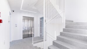 Escadaria moderna com guarda-corpo de metal, porta que dá para um elevador e interior limpo e branco.
