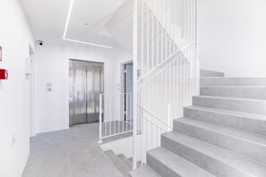 A modern staircase with a metal railing, a door leading to an elevator, and a clean, white interior. - Nua Boutique Apartaments 2 Towncentre, Finale Ligure, Italy (Finale Ligure)