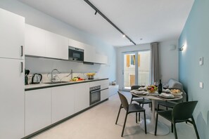 A modern kitchen with white cabinets, a microwave, and a dining area with a table set for two. - Nua Boutique Apartaments 2 Towncentre, Finale Ligure, Italy (Finale Ligure)